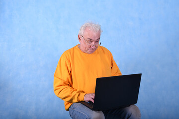 An elderly gray-haired man of retirement age at a laptop on a blue background
