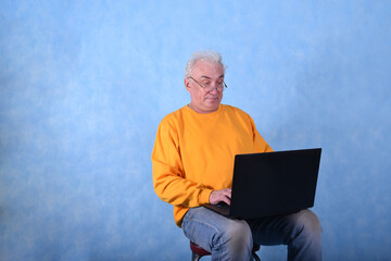 An elderly gray-haired man of retirement age at a laptop on a blue background