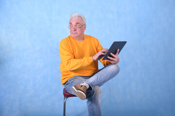 An elderly gray-haired man of retirement age with a tablet computer in his hands on a blue...
