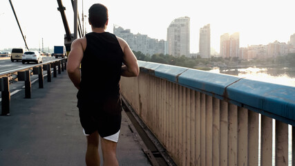 Fototapeta na wymiar back view of athletic mixed race man running on city bridge over river.