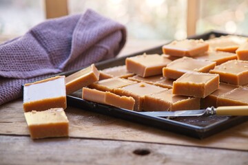 Homemade fudge squares on a baking sheet in warm sunlight on an old wooden table