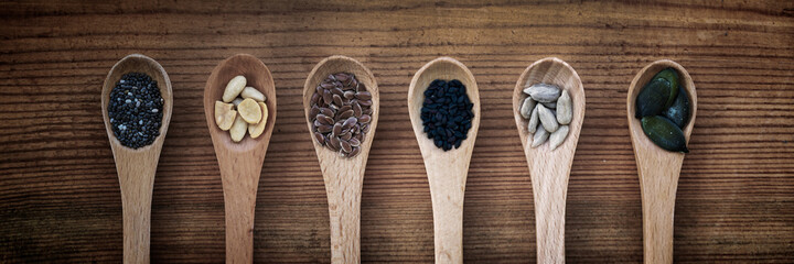 Set of organic seeds in spoons on panoramic wooden background, healthy natural food and nutrition concept