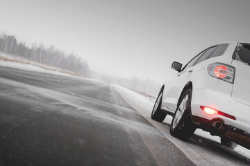 Fototapeta na wymiar White car on the icy empty road in the blizzard. Travel.