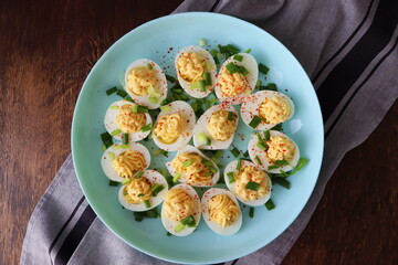 Deviled Eggs sprinkled with paprika and chopped green onion on a green plate on a woodene table . Top view