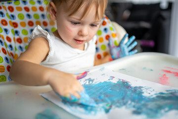 Cute little girl painting with fingers at home. Creative games for kids. Stay at home entertainment