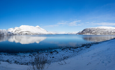 View at the fjord in the Atlantic Ocean with a snowy field in the polar area and mountains covered in snow near Tromso Norway