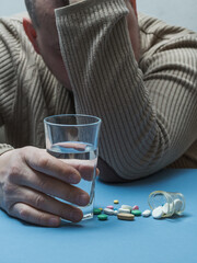 The man hides his face with his hands, the gesture symbolizes trouble, medicines and a glass of water are on the table in front of him.