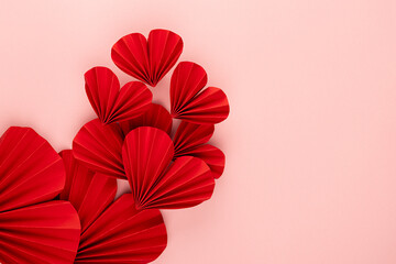 Valentine day background with flow of flying red paper ribbed hearts on soft light pink background as festive backdrop, top view, copy space, border.