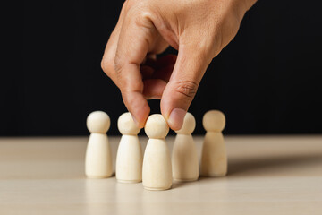 Wooden figures human was chosen leadership of teamwork. man's hands are select wooden puppet to...
