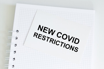 text new covid restrictions on a card that sits on a blank notebook on a table, a medical concept