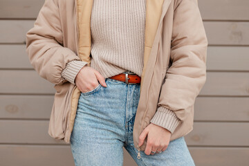 Woman in fashion outerwear with vintage beige knitted sweater, stylish blue jeans and jacket near a...