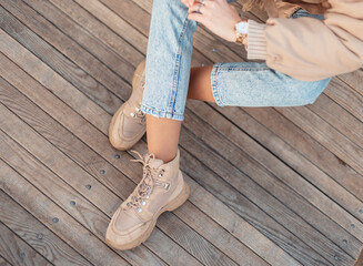 Fashionable girl with fashion winter outerwear in blue classic jeans and stylish leather beige shoes sits on a vintage wooden floor