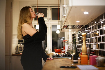 young woman in black cocktail dress drinking champagne in the kitchen