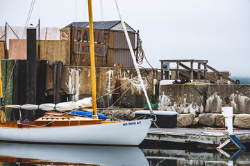 Sailboat docked near rustic shipyard on cloudy day in small seaside town