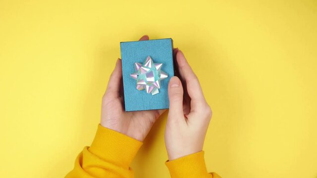Hands of a young woman open a blue gift box with keys to a new property with a keychain in the form of a house on a yellow background