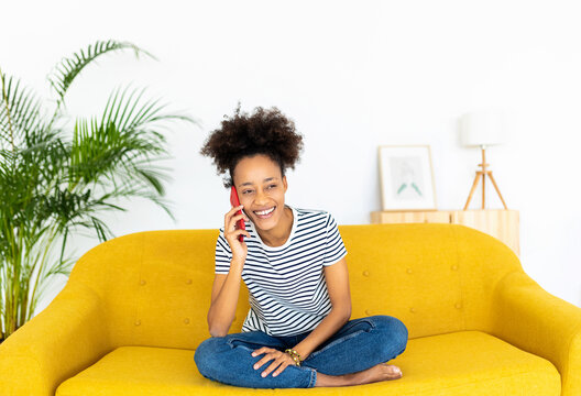 Mixed race african american girl teenager using mobile phone while sitting on sofa at home - Cheerful millennial female talking on smartphone - Youth and technology