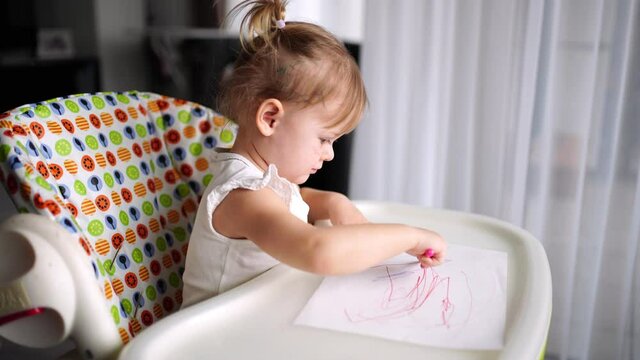 Cute little girl painting with red pencil at home. Creative games for kids. Stay at home entertainment
