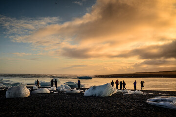 Silhouette of tourists enjoying the sunset amidst the remains of melted icebergs at the black beach...