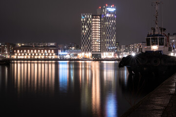 A view from the port across the river. Tall building casting reflections on the calm water.