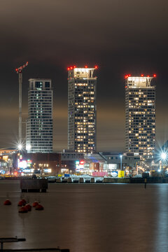 Three modern skyscrapers standing tall next to the river on a cloudy night.