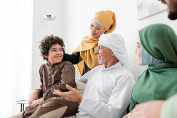 mature muslim man in turban talking to arabian grandson near happy interracial family.