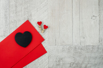 Black heart and red envelopes on gray wooden background, top view with copy space, gothic style