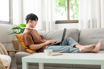 Technology Concept The man that is putting on glasses leaning his back on the dark yellow while focusing on the laptop’s screen