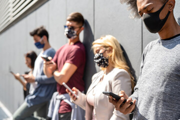 People using smartphone covered by mask on omicron variant wave - Worried guys and girls watching news on mobile devices - College students breaking at university campus - Focus on lower right phone