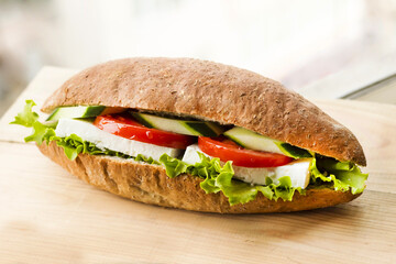 A sandwich with tomato, cucumber, feta cheese, lettuce on wooden board