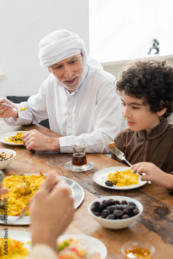 Wall mural muslim man eating pilaf with arabian grandson during family dinner.