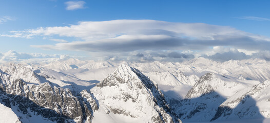 Aerial Panoramic View of Canadian Mountain covered in snow. Sunny winter season with cloudy sky art...