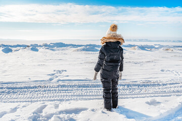 Rear view of a little girl alone in the middle of a snowy desert on a frozen river on a sunny winter day