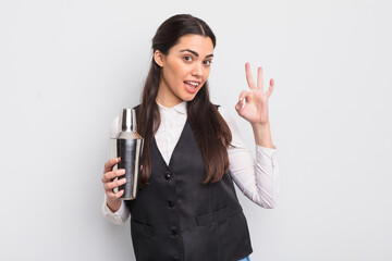 pretty hispanic woman feeling happy, showing approval with okay gesture. barman cocktail concept