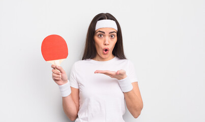 pretty hispanic woman looking surprised and shocked, with jaw dropped holding an object. ping pong...