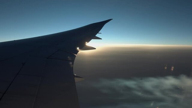 Airplane Wing and jet streams in flight from window, sunset sky, jet streams highlighted by sunset Sun