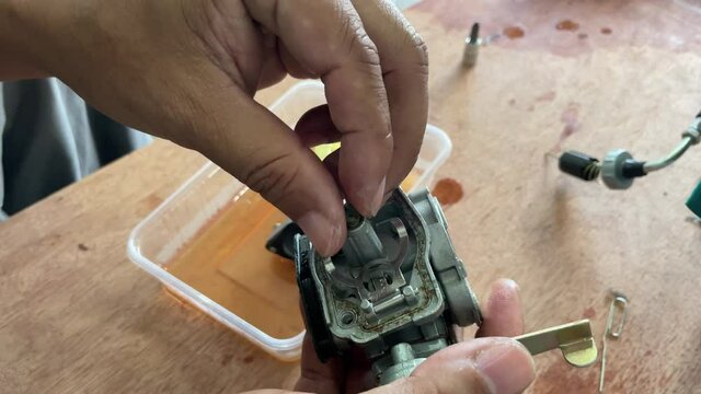 A young man is repairing a small two-stroke engine used for farming. disassemble the parts cleaning the carburetor Reassemble and test 