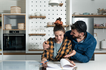 Young creative couple business owners and partners writing ideas for increasing company strategy and profit. Man and woman standing in the kitchen working on the new project with inspiration.