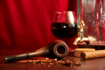 Bottle of brandy with a glass, smoking pipe and cigar on the wooden desk. Business man cabinet