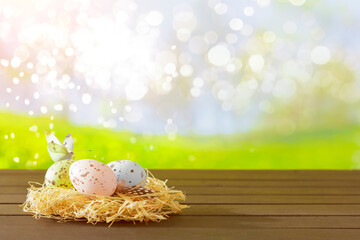 Easter eggs painted in muted colors on a hay nest in front of a springtime garden background, copy space for Happy Easter text.