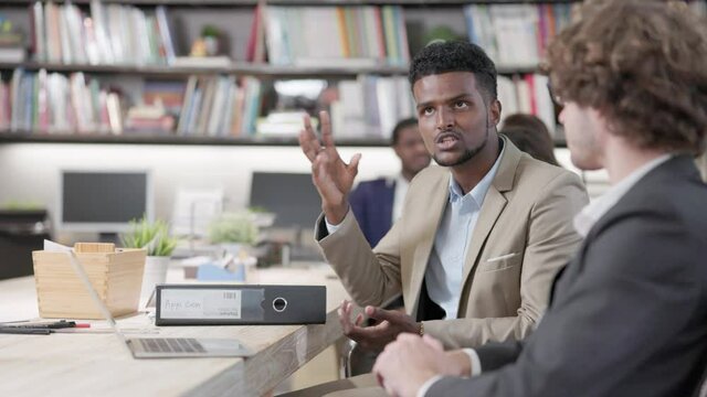 Two male coworkers in the office conversing and working together at work, happy businessmen teammates discussing computer business project brainstorming in corporate teamwork