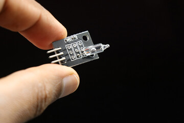 Mercury tilt switch sensor module held in hand isolated on black background, Electronic sensors for...