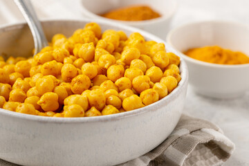 IIndian traditional dish - crispy roasted chickpeas with spices curry powder, garam masala, and turmeric in a light bowl on a white table, selective focus, low depth of field