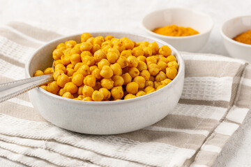 Indian traditional dish - roasted chickpeas with spices curry powder and turmeric in a light bowl on a striped napkin on white table. Close up