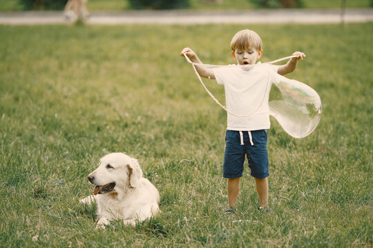Little boy making a giant soap bubbles while playing with his dog on a grass