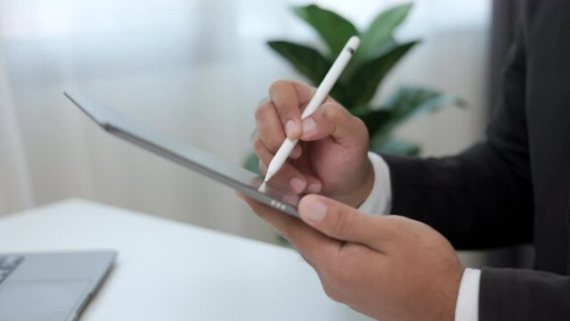 Businessman using stylus pen signing contract on digital tablet at work in office Indoors. Close up hand write business agreement of contract. Electronic Signature on Tablet Computer.
