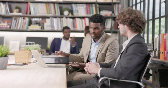 Two male coworkers in the office conversing and working together at work, happy businessmen teammates discussing computer business project brainstorming in corporate teamwork