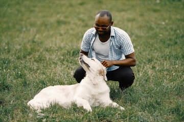 Black american man in a sunglasses sitting with has dog on a grass