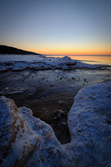 colorful beautiful sunset at sea in winter with snow on the beach