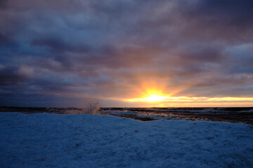 ice splashes at the sea on a cold winter sunset with snow and clouds in the sky