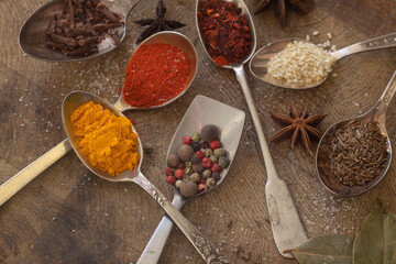 7 metal spoons on a wooden surface and with different spices such as turmeric, smoked paprika, dried paprika,salt, zira . 
